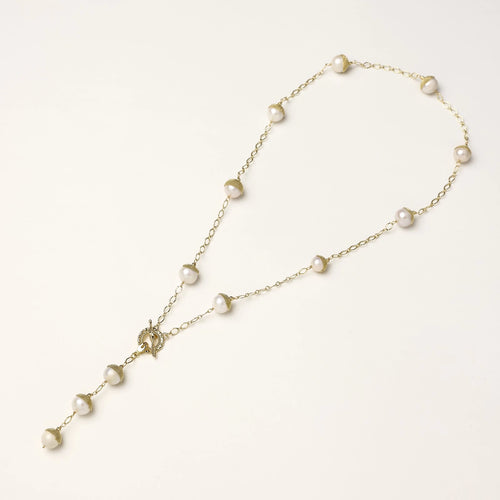 Gold-plated lariat necklace with baroque pearls and textured caps on cream background, showing adjustable Y-shaped design.