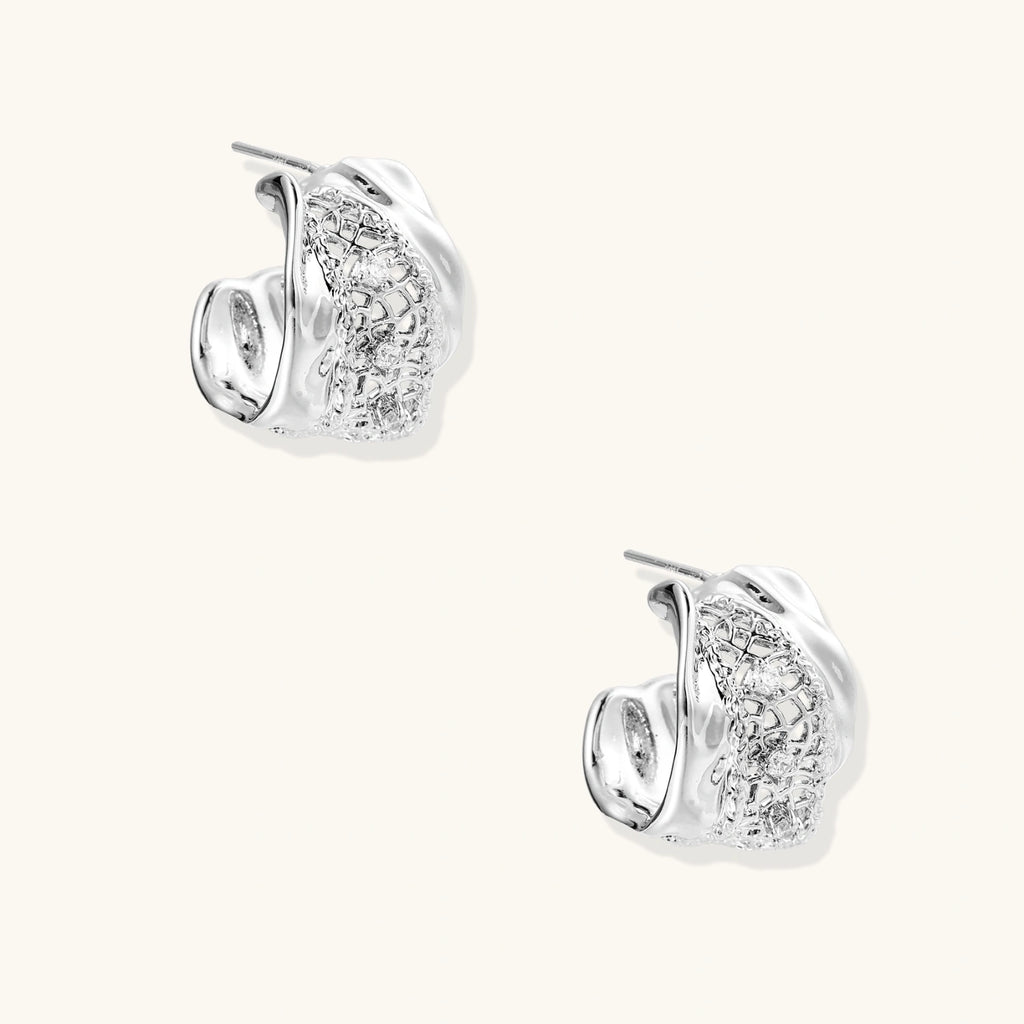 Close-up of sculptural hoop earrings with lattice center band and smooth twisted edges in white gold-plated brass with zirconia