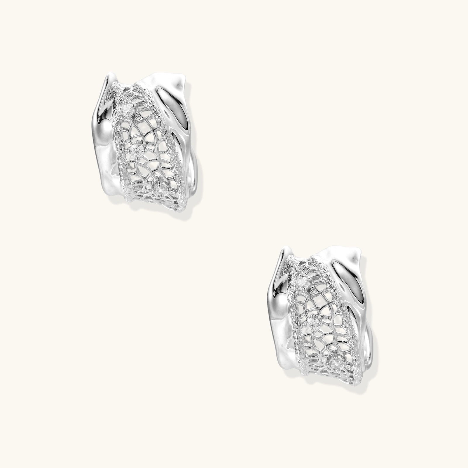 Close-up of sculptural hoop earrings with lattice center band and smooth twisted edges in white gold-plated brass with zirconia