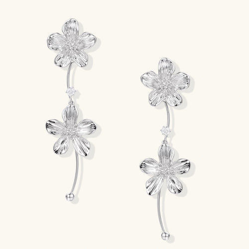 Silver-white asymmetric earrings with textured flower petals and crystal centers on cream background