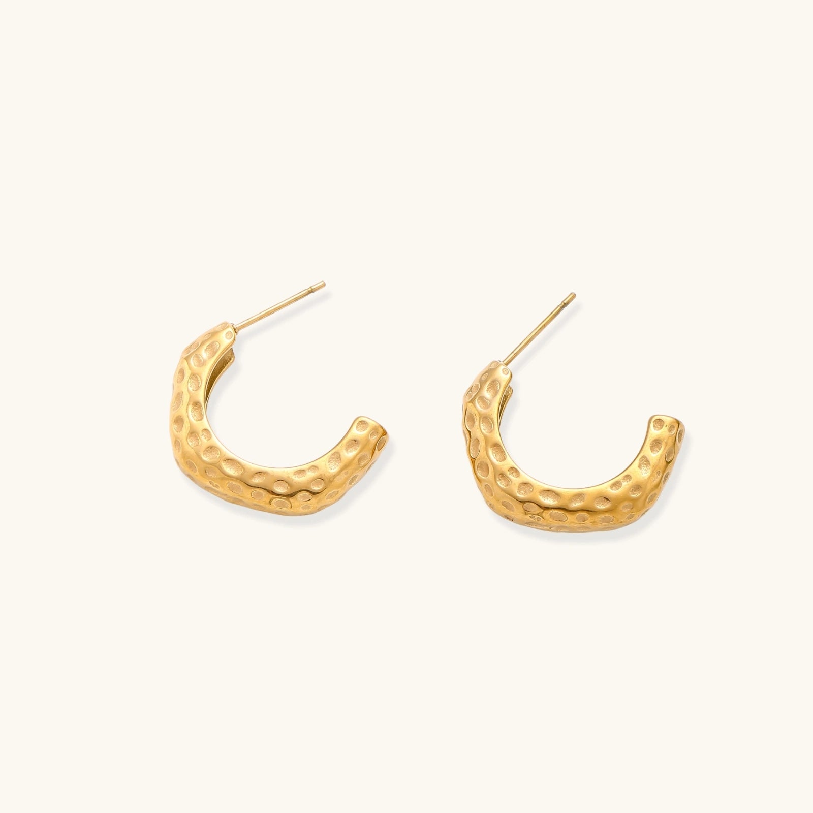 Gold-toned hoop earrings with hammered dimpled texture and post closure on cream background