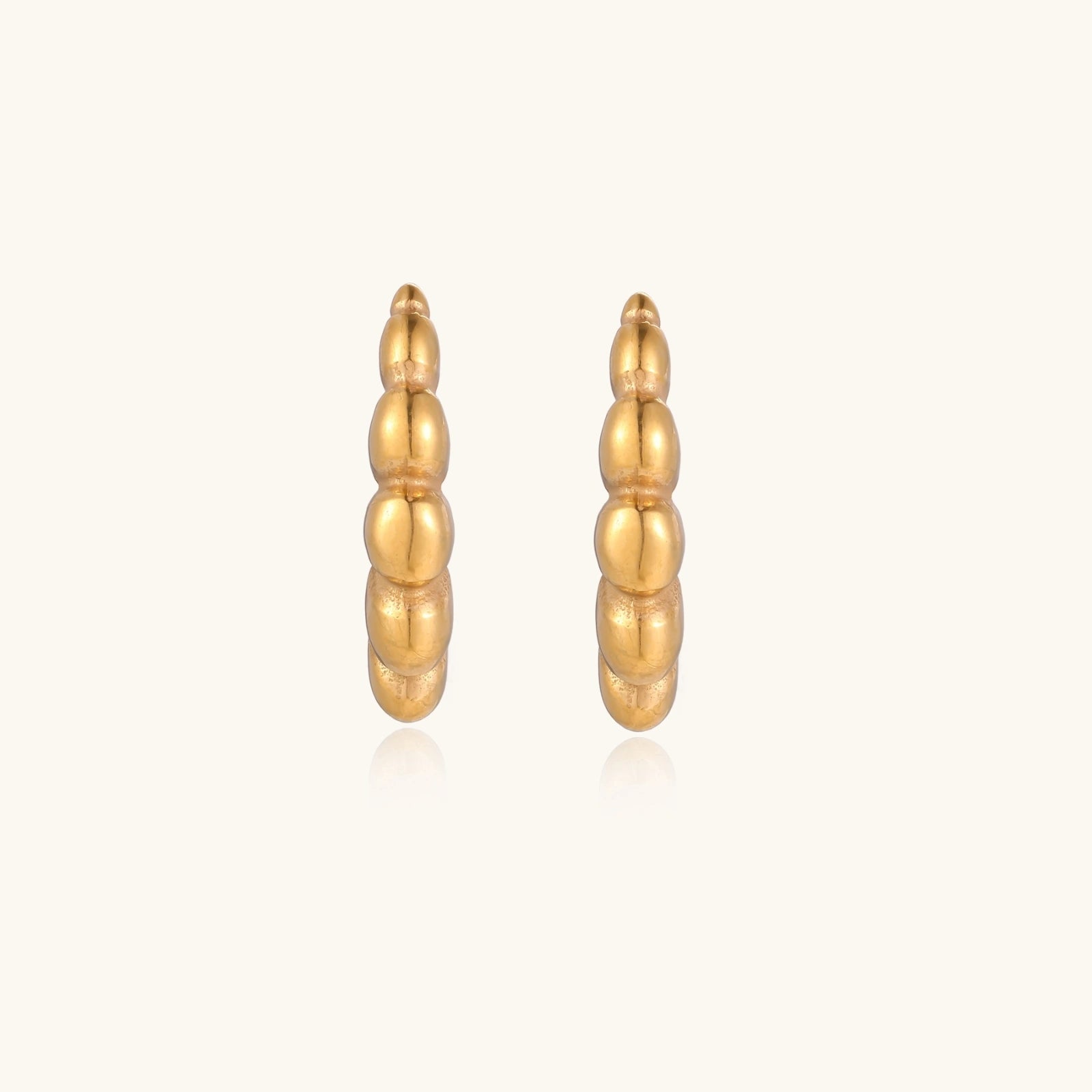 Gold-plated chunky hoop earrings with ridged bubble texture on cream background