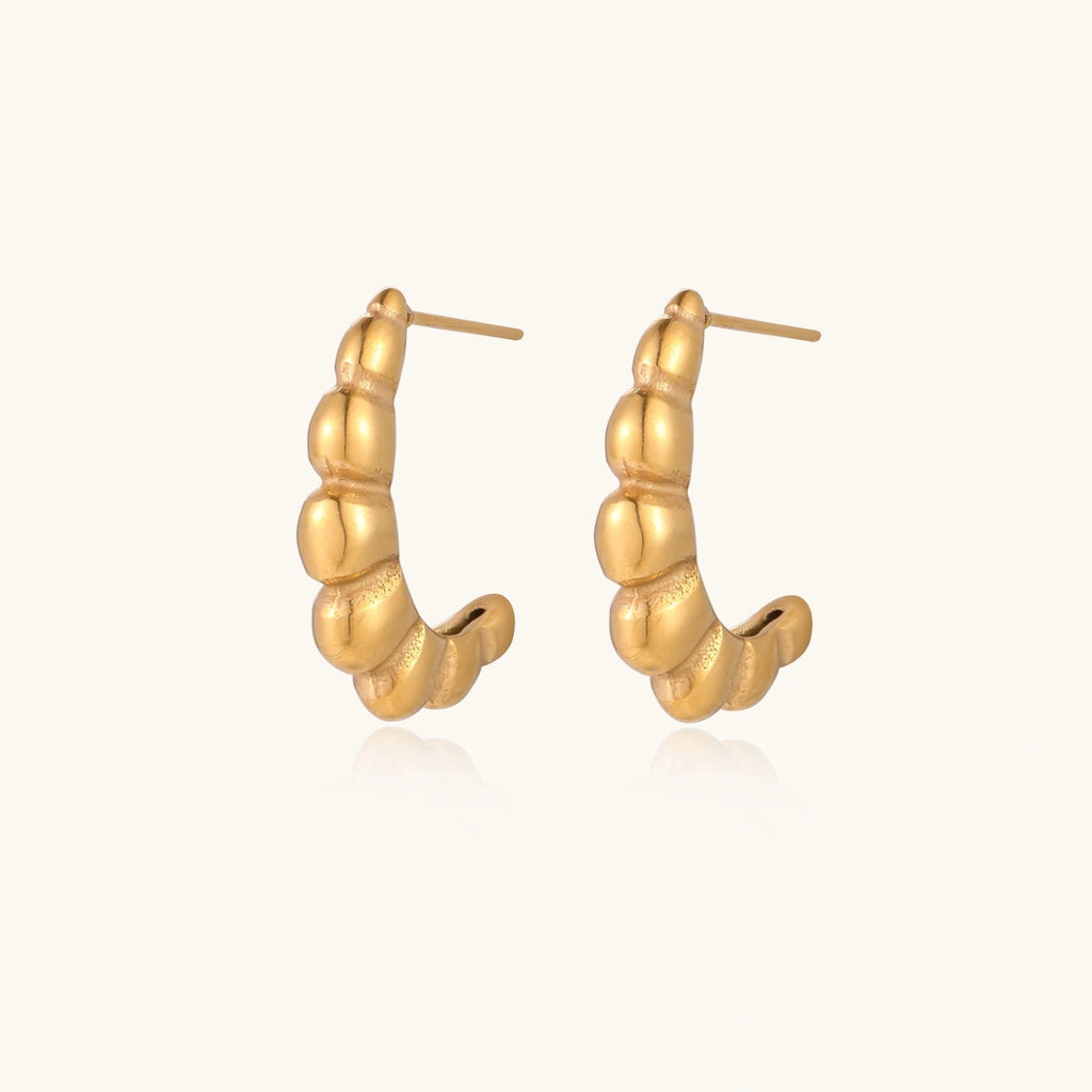 Gold-plated chunky hoop earrings with ridged bubble texture on cream background